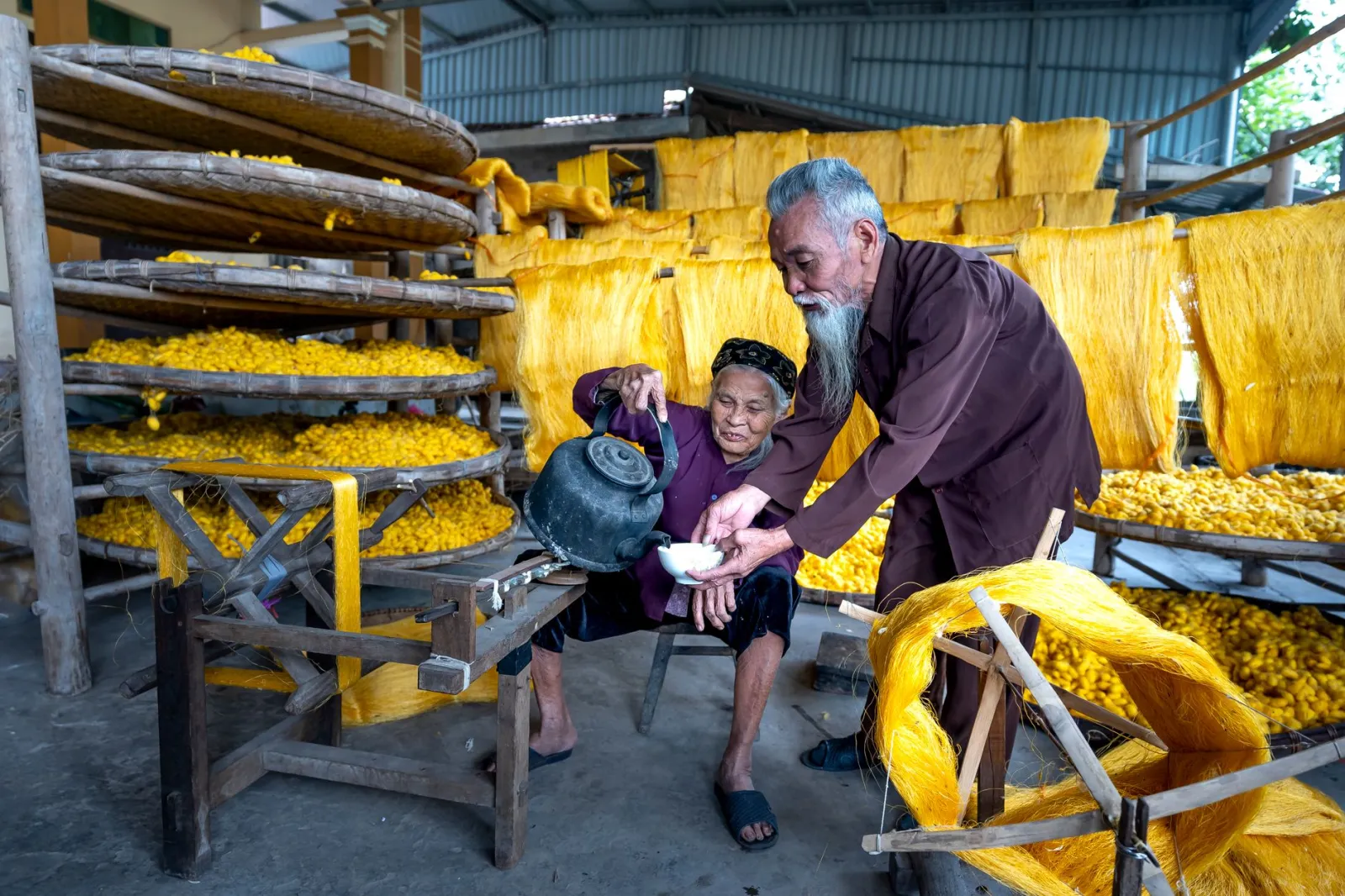 Elderly couple working on traditional silk production process indoors.