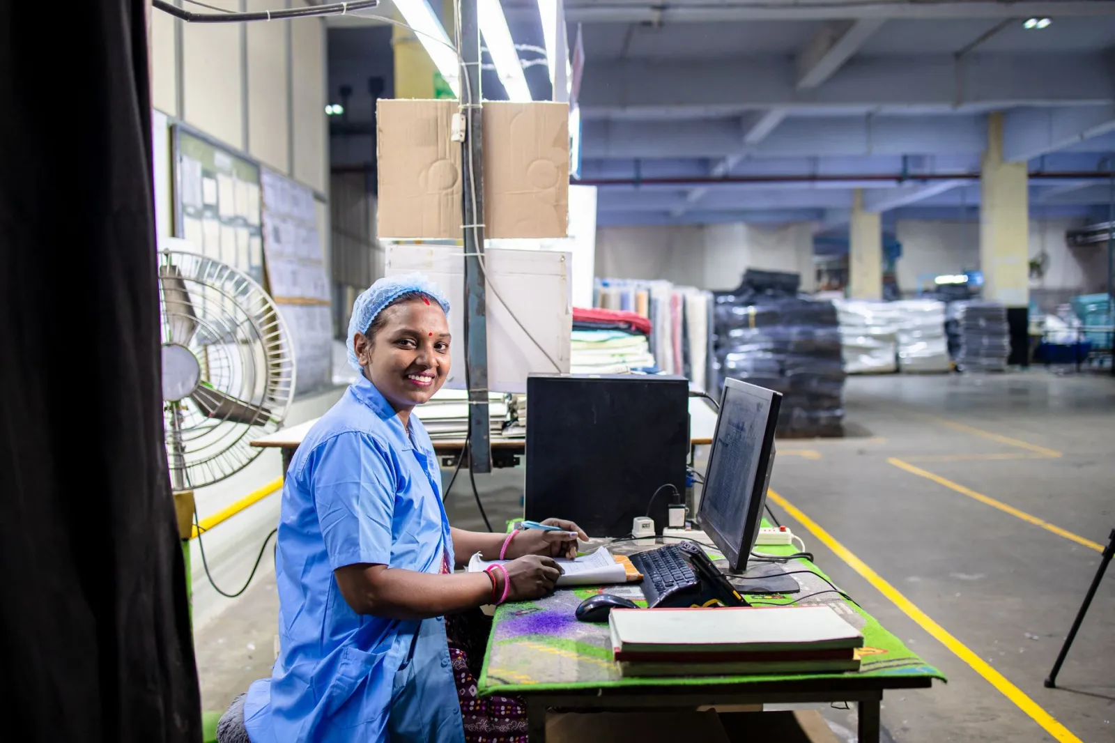 A cheerful textile factory worker at her desk in an industrial setting, showcasing the dynamic work environment.