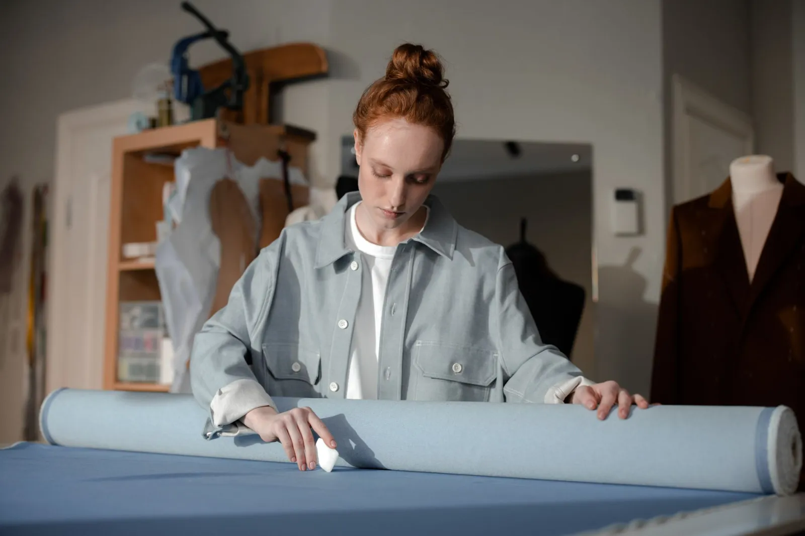 Woman dressmaker marking fabric with chalk in a fashion workshop setting.