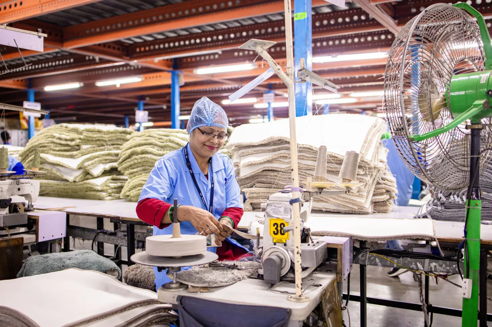 Smiling Indian textile worker at sewing machine in factory setting.