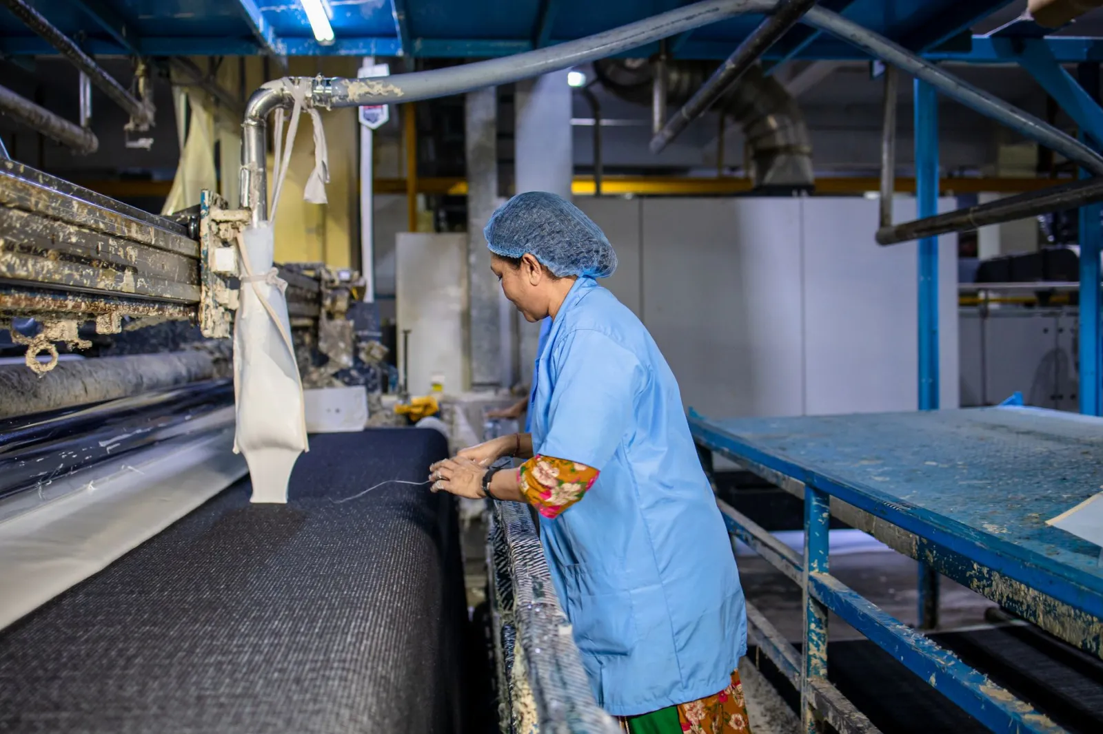 A female textile worker operates machinery in a factory, showcasing industrial production.