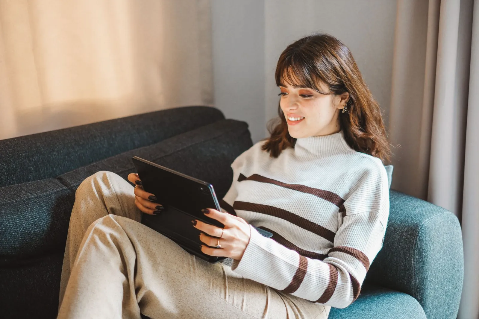 Smiling woman using a tablet on a cozy sofa, enjoying leisure time indoors.