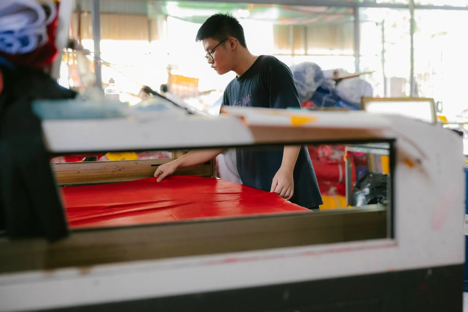 A focused worker examines fabric in a busy textile workshop.