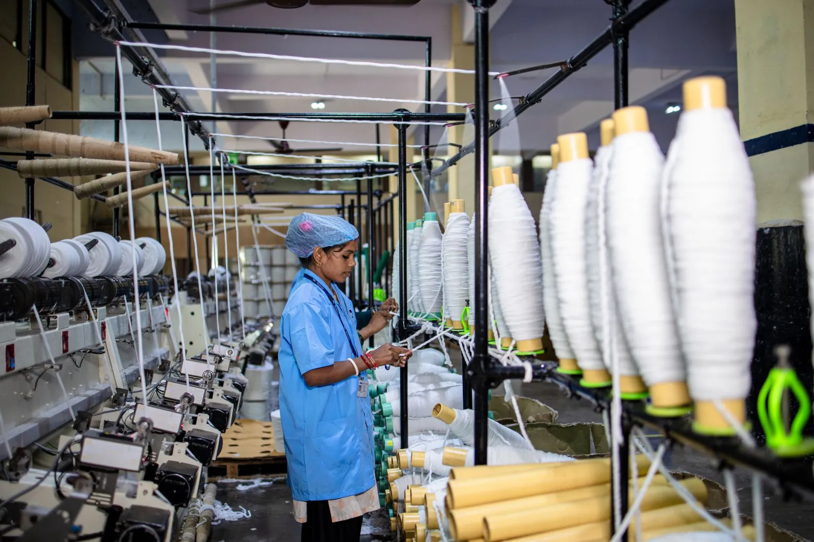 Female worker operates machinery at textile factory, focusing on spools of thread.