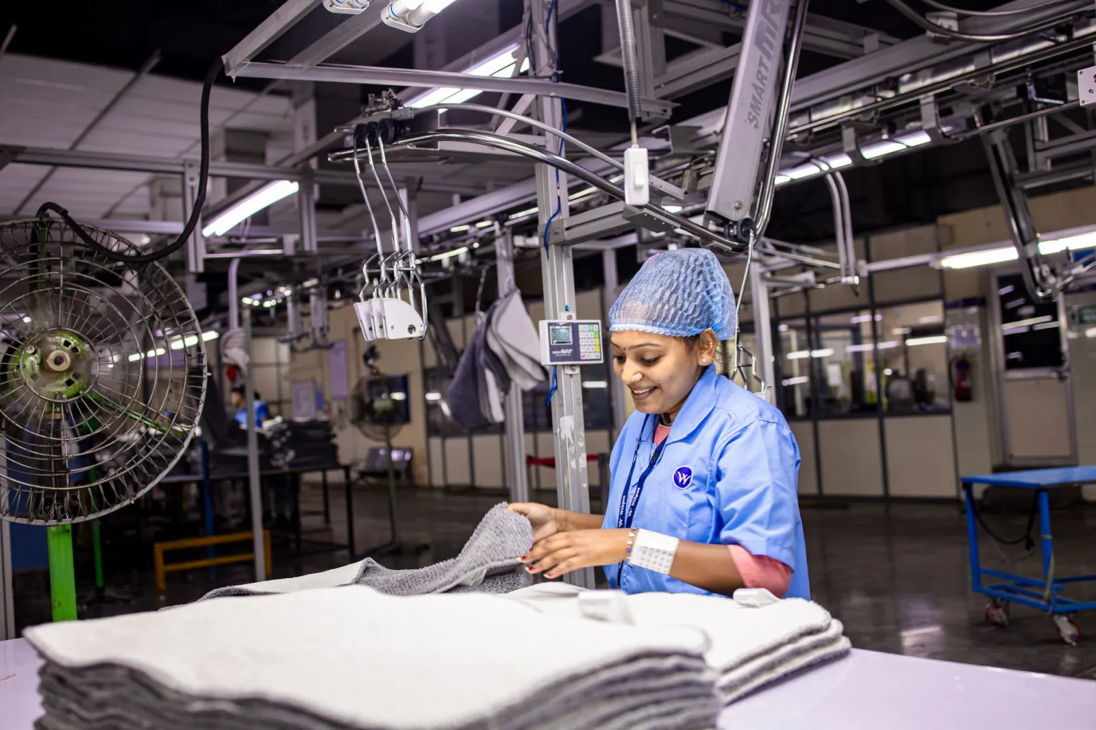 A female textile worker smiling while sorting fabrics in a modern factory setting.