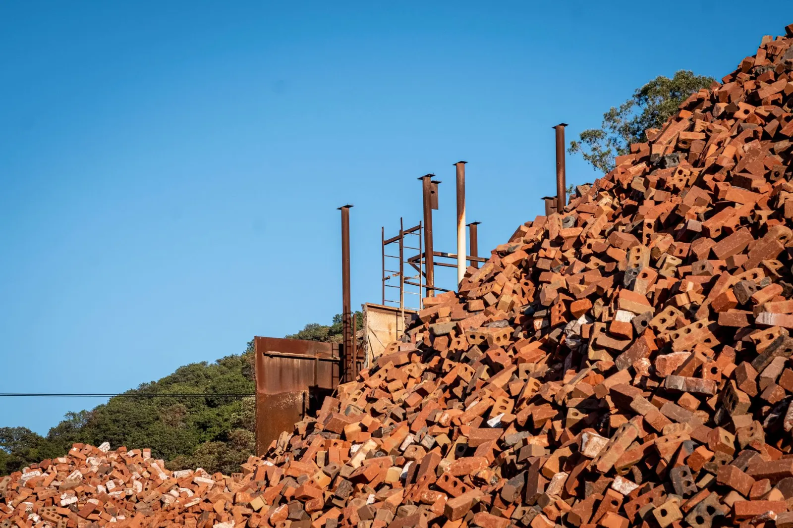 A towering pile of terracotta bricks under a clear sky at an outdoor construction site.